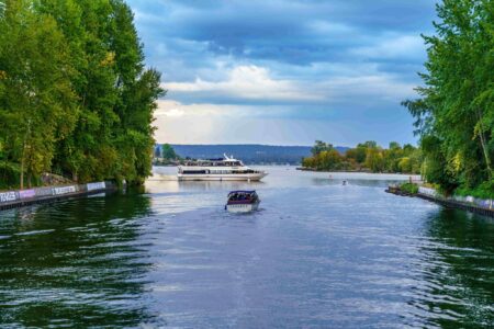 A small motorboat travels down a tree-lined river toward a larger boat.