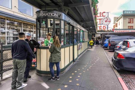 Four people stand and talk near a market information booth at Pike Place Market.