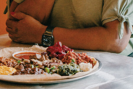 A person wearing a grey shirt sits at a table with a large plate filled with food in front of them.