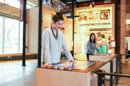 Two women interact with educational displays in a museum exhibit titled 