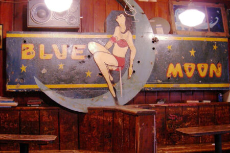 A vintage sign inside a dimly lit bar features a retro-style illustration of a woman sitting on a crescent moon. The words 