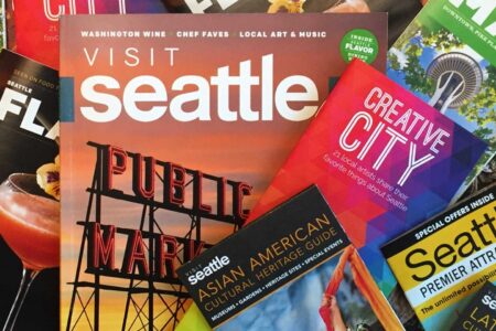 A collection of colorful travel brochures and maps for Seattle, featuring images of landmarks and cultural attractions like Pike Place Market. Prominent titles include 