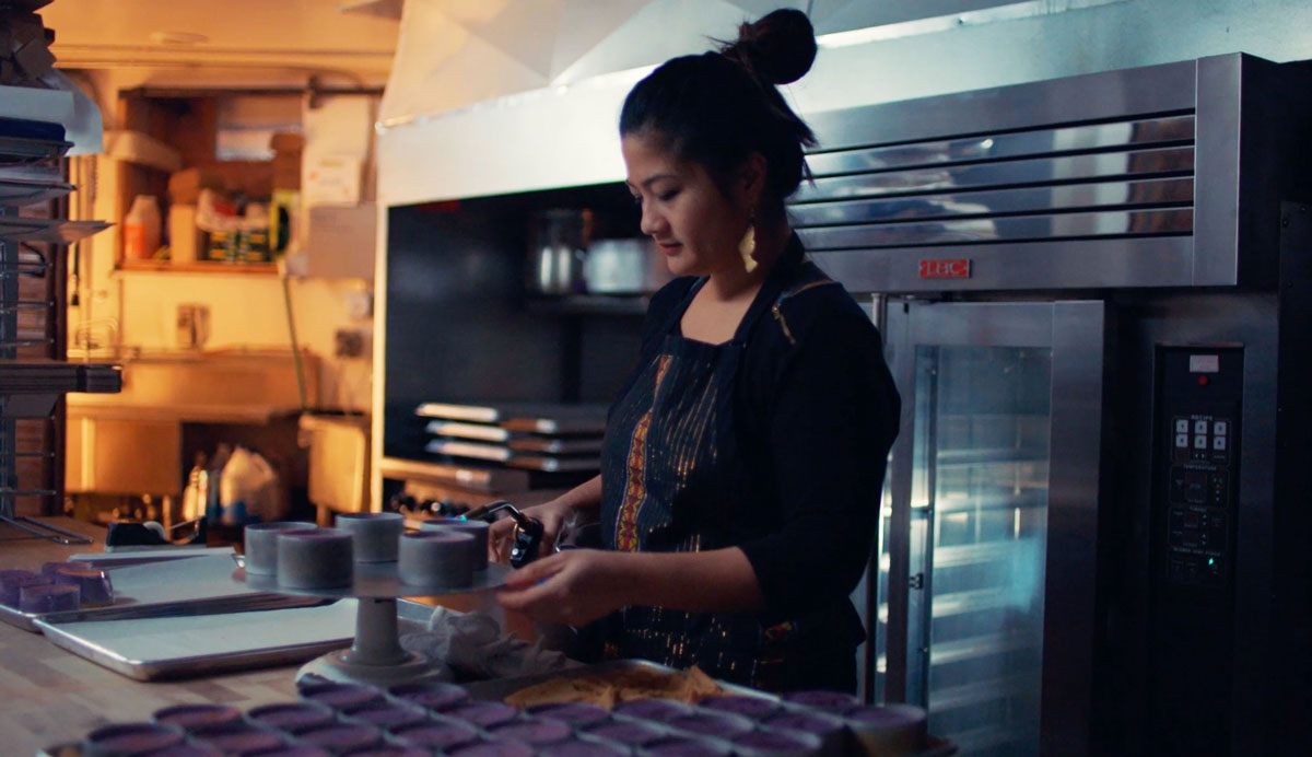 A person standing in a kitchen creating purple cheesecakes and placing them on a tray.