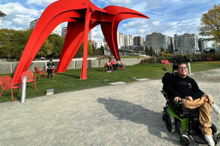 A person in a wheelchair sits in the foreground with a large orange sculpture in the behind them and the Space Needle in the background.