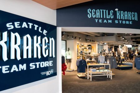 Entrance to the Seattle Kraken Team Store, featuring bold signage and a display of merchandise inside, including clothing and accessories. The interior is well-lit and arranged with sports-related items.