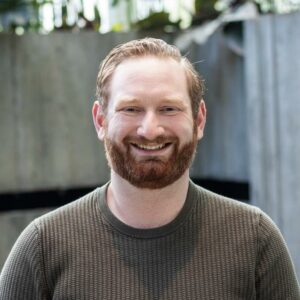 A redheaded white man smiles at the camera
