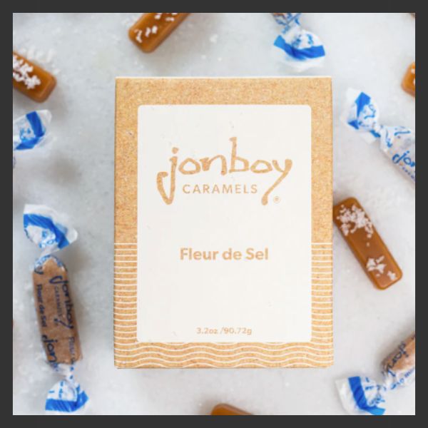 A box of Jonboy Caramels labeled "Fleur de Sel" is surrounded by individually wrapped caramel candies on a white surface.
