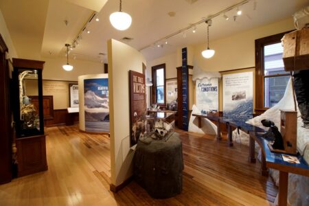 A well-lit museum exhibit featuring informational panels and displays on extreme conditions in nature. The room has wooden floors and white-paneled walls, with various objects and images related to the theme arranged neatly for visitors.