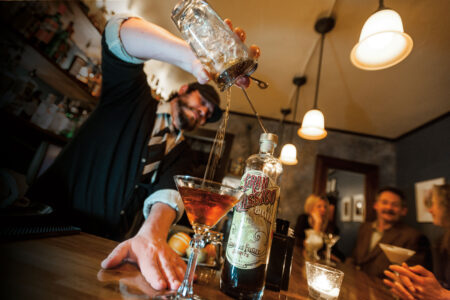 A bartender pours a drink from a bottle labeled 
