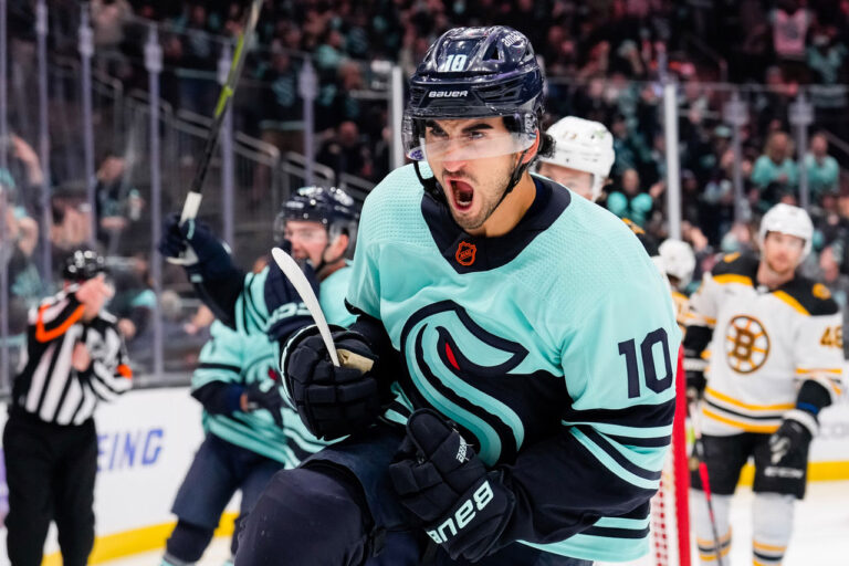 A hockey player in a light blue jersey celebrates on the ice with enthusiasm, embodying the electric energy of things to do in Seattle. Other players and a referee are visible in the background as the audience cheers from the stands.
