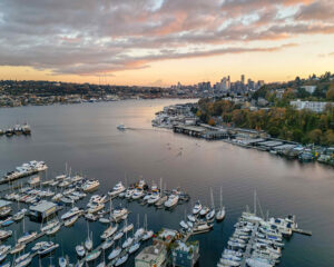 Birds-eye view of a lake with docked boats in the foreground and a sunset in the background.