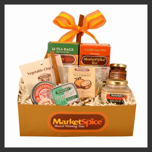 A MarketSpice gift basket containing tea bags, tea cookies, honey, jam, mints, and vegetable chips, arranged in a box with shredded paper and topped with an orange and yellow ribbon.