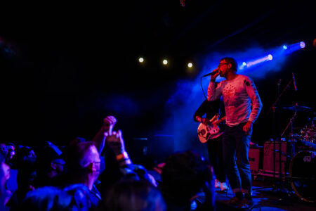 A live band plays on stage at The Crocodile music venue. A crowd cheers along as colorful stage lights hit the performers.