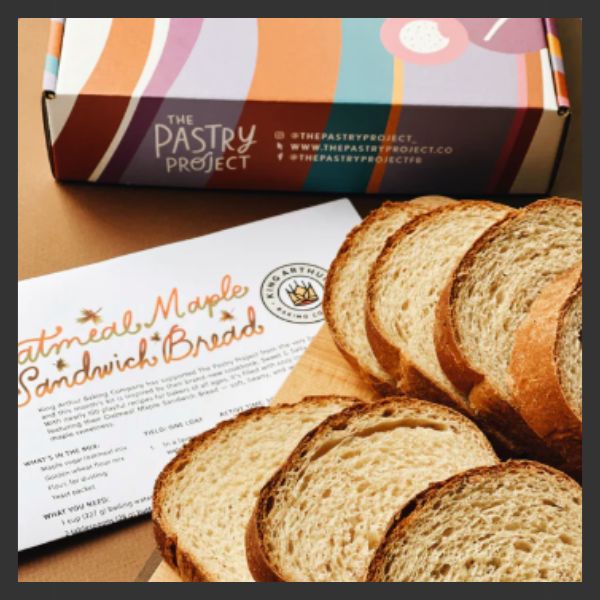 Sliced oatmeals and maple sandwich bread on a table next to an information card and a colorful box labeled "The Pastry Project.