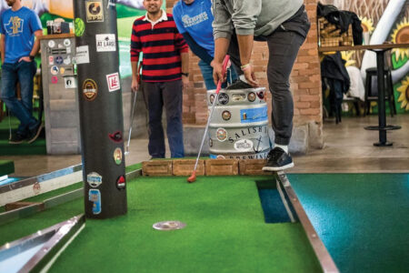 A photo of people playing mini golf. One person stands on the green while friends in the back look on.