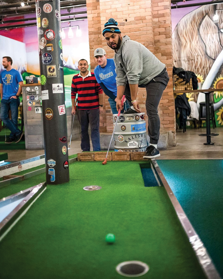 A photo of people playing mini golf. One person stands on the green while friends in the back look on.