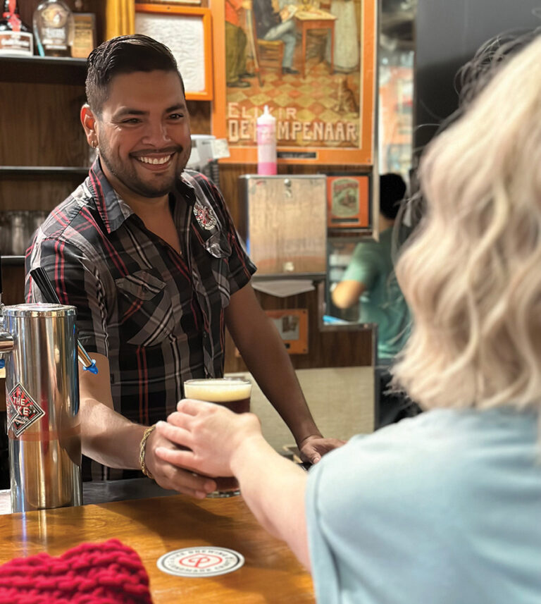 A man hands a woman in a blue shirt a beer across a bar top.