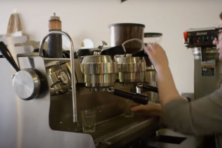 A woman using a silver espresso machine to make coffee in a cafe.