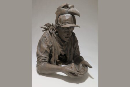 A clay sculpture of a person wearing a bird-shaped hat, holding a small bird in their hands. The figure has a serious expression and a bird perched on their shoulder, and is dressed in casual clothing.
