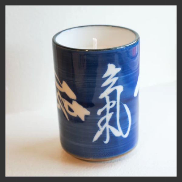 A blue ceramic candle holder with white Chinese or Japanese characters painted on it, containing a white candle.