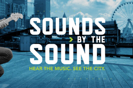 A black and white image with blue accents shows a guitarist and a singer with a city skyline and Ferris wheel in the background. Text reads: "Sounds by the Sound. Hear the Music. See the City." Featuring logos for Revolt and Visit Seattle.