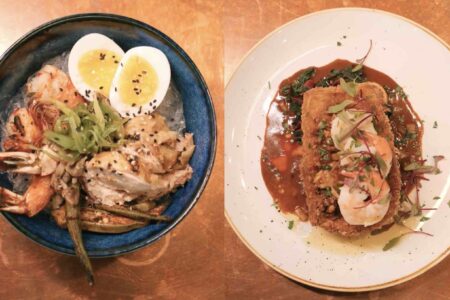 A top-down view of two dishes. On the left, a bowl with grilled seafood, half a boiled egg, rice, and vegetables. On the right, a plate with fried shrimp on a bed of greens, topped with sauce and herbs. Both are presented on a wooden table.