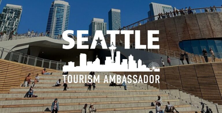 People sit and walk on wide wooden steps in front of a modern building in Seattle, with tall city buildings in the background. Overlaid text reads: "Seattle Tourism Ambassador" with a Seattle skyline graphic.