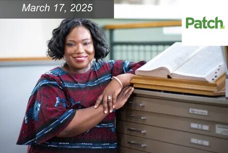 A person in a patterned dress leans on a cabinet, smiling, with an open book on top.