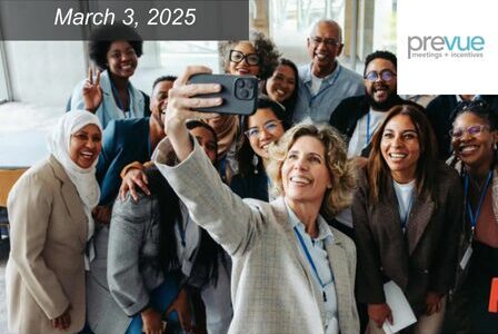 A group of diverse smiling and taking a selfie together. One person holds the phone, and everyone is gathered closely.