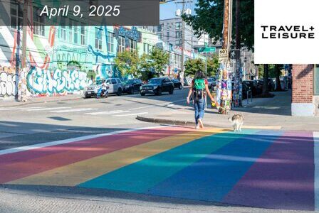 A person walks a dog across a rainbow-painted crosswalk in a colorful, graffiti-covered urban area.
