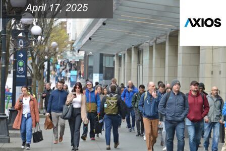 A diverse group of people walk along a busy city sidewalk under a glass canopy.