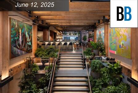 A modern, plant-filled interior space with wide stairs, colorful art on wood-paneled walls, and a bar area in the background.