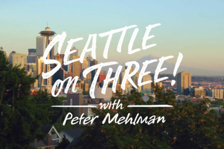 A cityscape of Seattle with the Space Needle and surrounding buildings. The text "Seattle on Three! with Peter Mehlman" is written across the image in bold, white letters. There are trees in the foreground and a clear sky above.