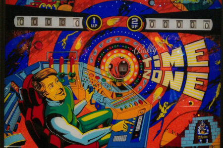 Vintage pinball machine backglass featuring a colorful sci-fi theme. A person operates a control panel with a cosmic portal in the background and the text 