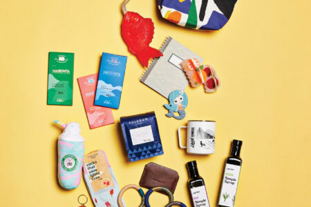A colorful flat lay of various items, including a patterned pouch, notepad, hair ties, socks, a toy, bath products, and coffee packets on a yellow background.