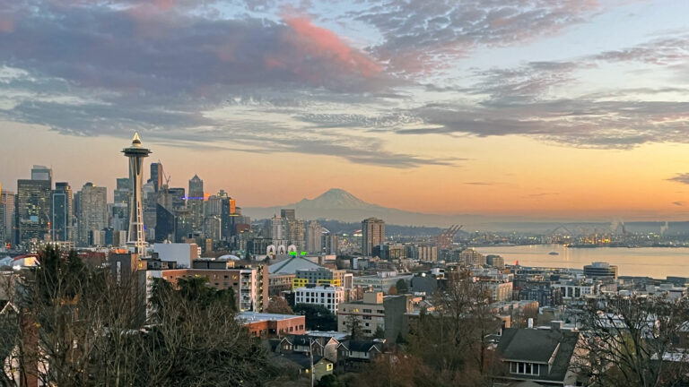 Seattle city skyline from Kerry Park at sunset, featuring the Space Needle with white string lights on top resembling a Christmas Tree.