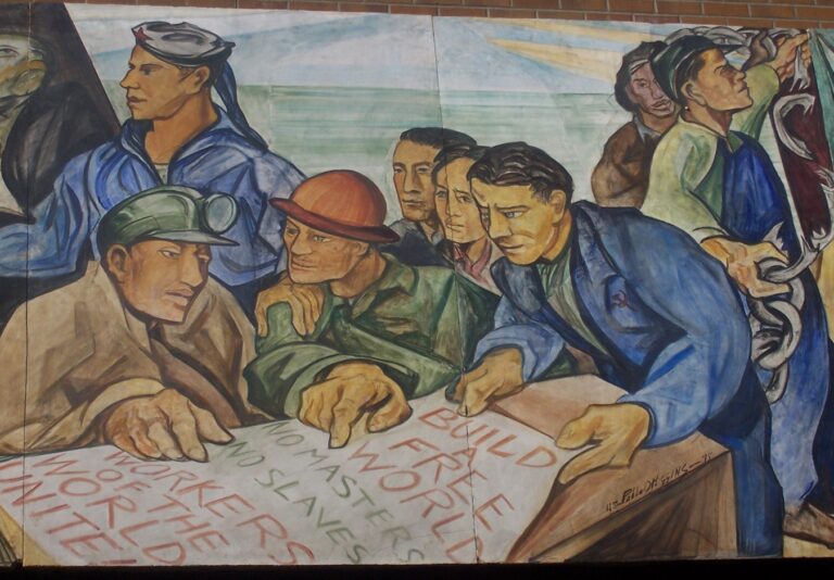 A mural depicting workers in various uniforms holding and reading a large document with "Build a free world" and "Workers of the world unite" written on it. The scene conveys unity and determination.