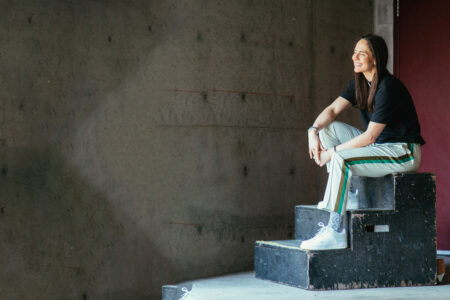 WNBA star Sue Bird sitting on a three-step stool, facing to the left and smiling.