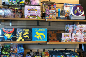 Shelves display various Pokémon trading card boxes and packs, including Elite Trainer Boxes, booster packs, and collection sets featuring colorful artwork and popular Pokémon characters.