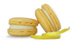 A photo of two yellow macrons with a curled lemon peel on the bottom right.