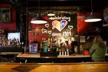 Interior image of a bar with a rainbow heart painted on the mirror and the words, "Celebrating Love since 1984"
