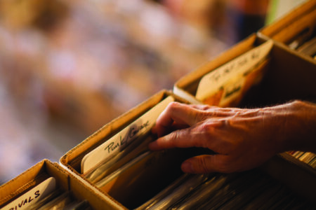 A hand reaches into a cardboard box filled with vinyl records, selecting an album labeled "Pink Floyd." The background is blurred, giving focus to the records and the hand's interaction with them.