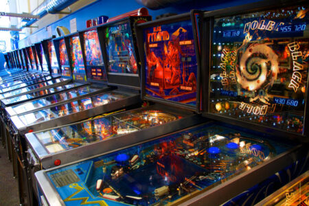 Six colorful pinball machines line a blue wall.