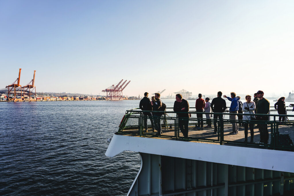 A group of people stand on the deck of a ferry boat surrounded by a green railing.