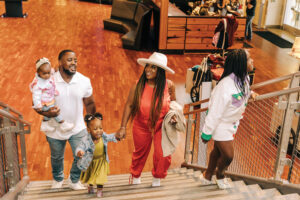 Two adults and three kids walk up grey stairs.