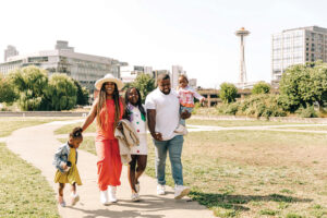 A family of five, including two adults and three children, hold hands and walk across a park.