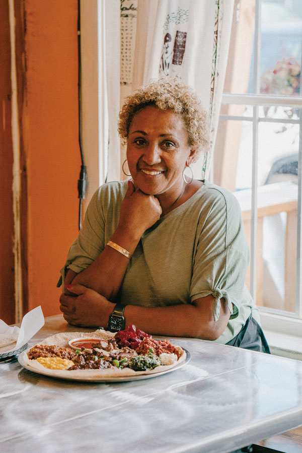 A person wearing a grey shirt sits at a table with a large plate filled with food in front of them.