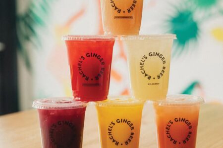 A pyramid of six colorful drink cups with transparent lids on a wooden table. Each cup has 
