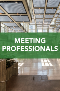 Spacious, modern lobby with large windows and ceiling lights. A green banner with white text in the center reads “MEETING PROFESSIONALS.”.