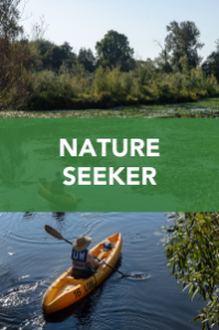 A person paddles a yellow kayak on a calm river surrounded by greenery, with sunlight filtering through trees. Text overlay reads "NATURE SEEKER" in bold white letters on a green background.